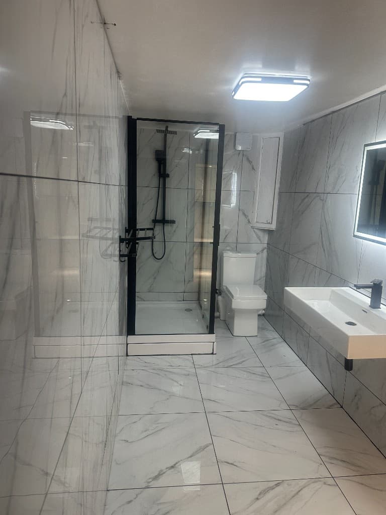 Finished bathroom with marble-effect wall and floor tiles, a glass shower enclosure and a wall-hung basin