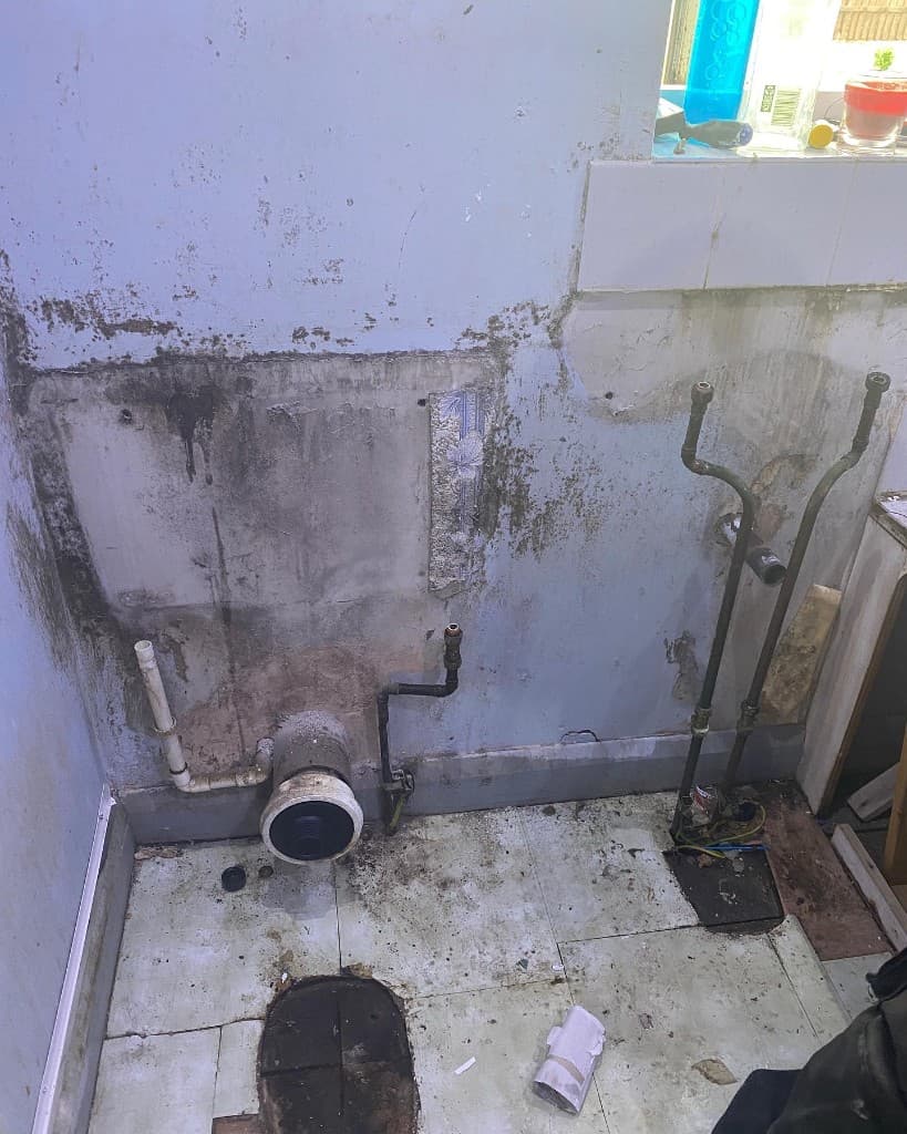 Bathroom before renovation, with exposed waste and pipework on stained walls