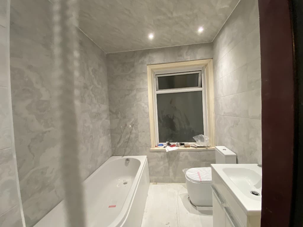 Bathroom tiling in progress around a bath, toilet and window