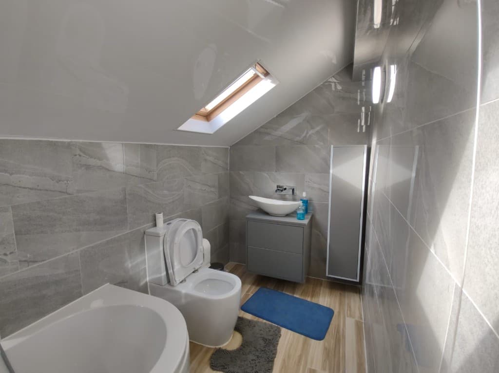 Finished loft bathroom with grey wall tiles, a vessel basin and a bath