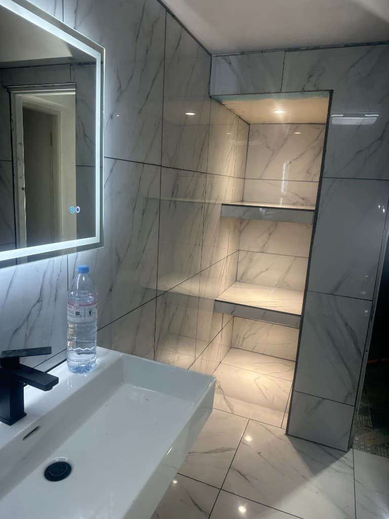 Marble-effect tiled bathroom with a lit niche, basin and black tap