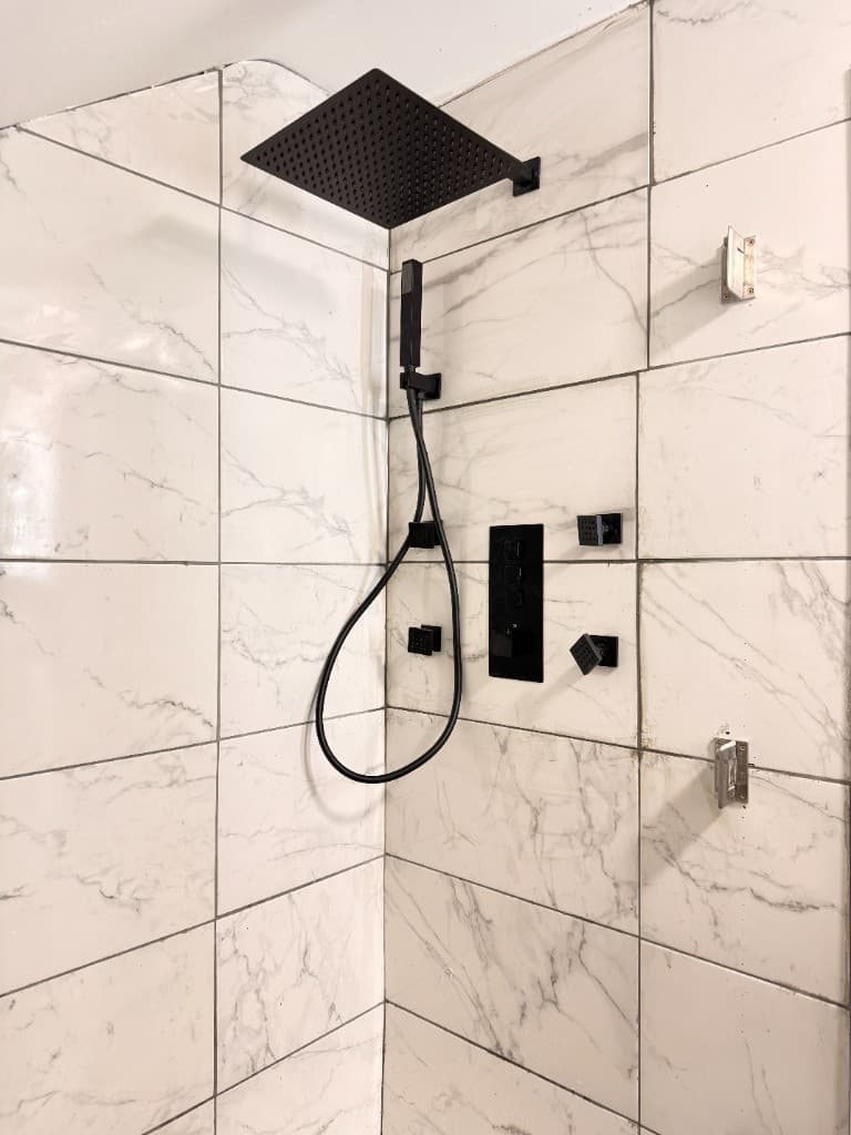 Marble-effect tiled shower with a black rainfall head, handset and valves