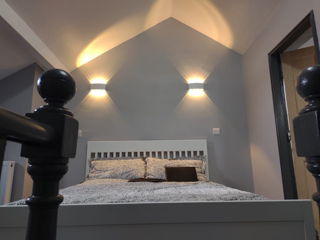 Finished loft bedroom with wall lights, painted walls and a made bed