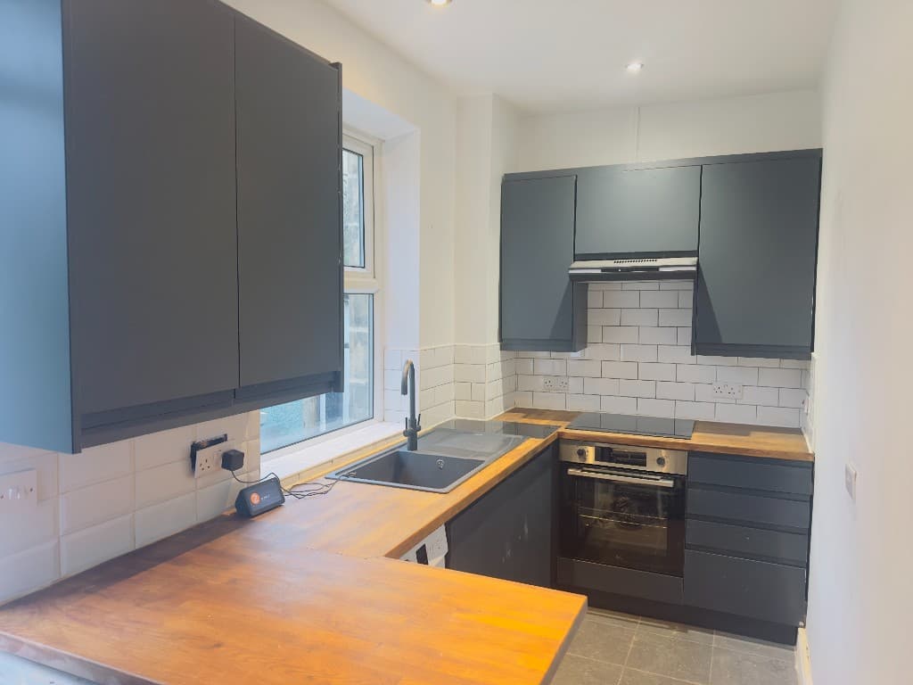 Kitchen with grey wall and base units, wooden worktops and a white metro-tile splashback