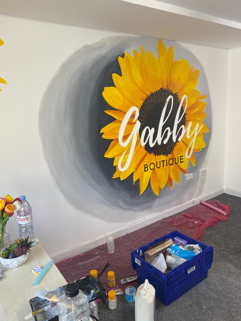 Hand-painted sunflower mural in progress, with the lettering taking shape